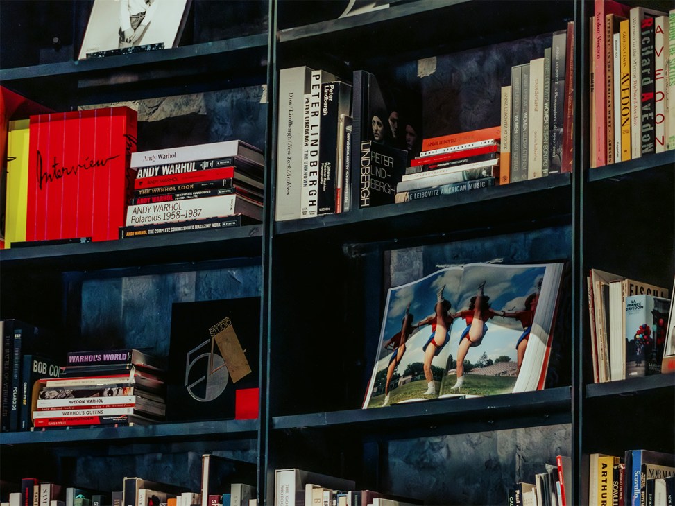 Dark shelving unit displaying rare fashion and art books, magazines, and photography publications with colored spines.