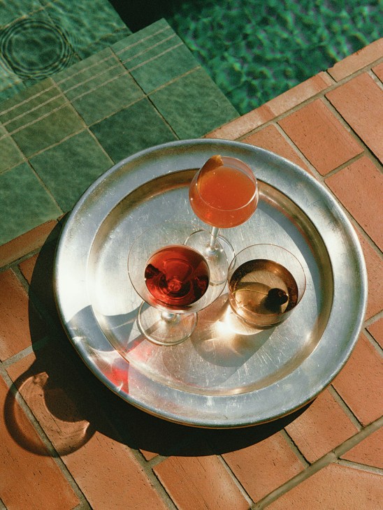 Three wine glasses filled with red and amber wines on a metal tray viewed from above on tiled floor.