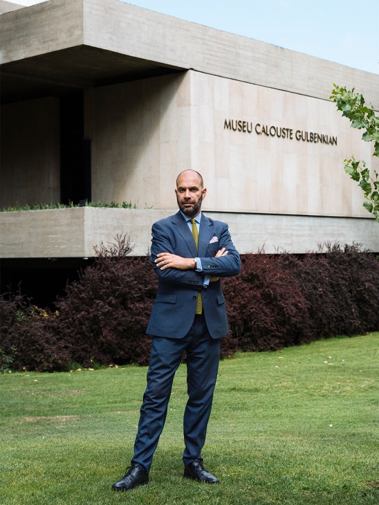Xavier Salomon, director of the Calouste Gulbenkian Museum, standing with arms crossed in front of the museum's concrete facade.