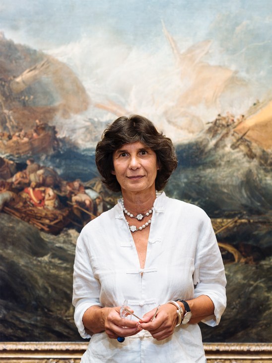 Luísa Sampaio, head of collections and senior curator of painting and sculpture, stands in front of a large classical landscape painting.