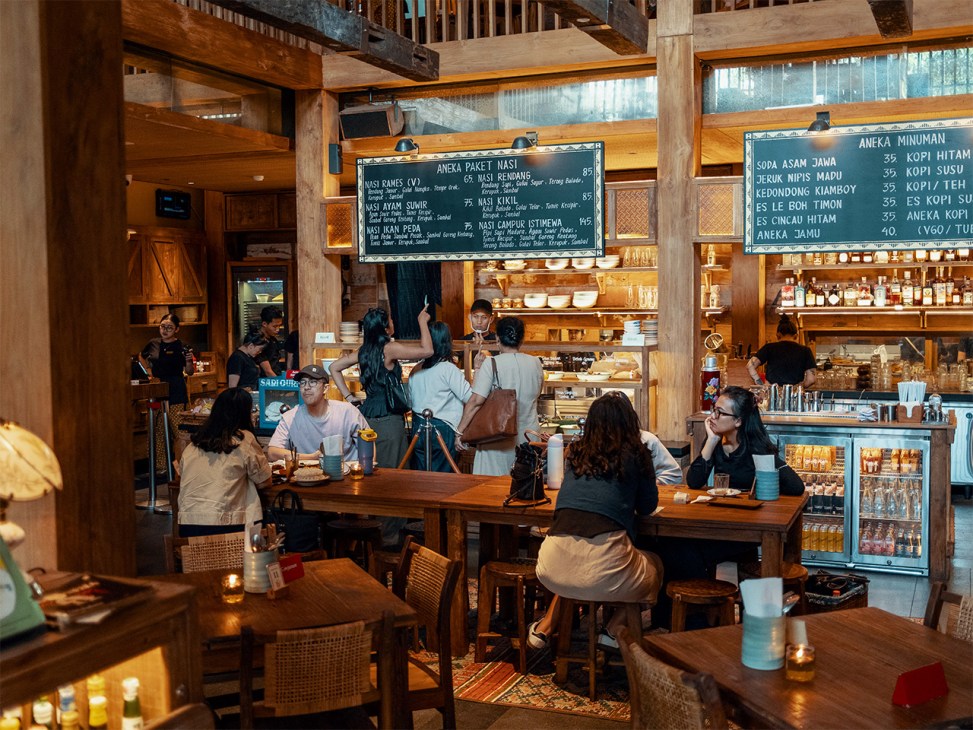 Interior of Salira restaurant showing a buffet-style warteg counter with menu boards and diners seated at wooden tables.