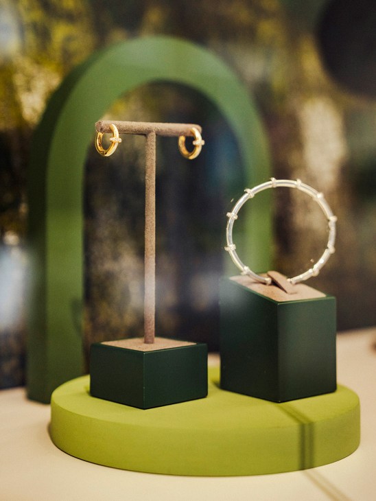 Gold hoop earrings and a spiky silver ring displayed on green and black presentation stands.