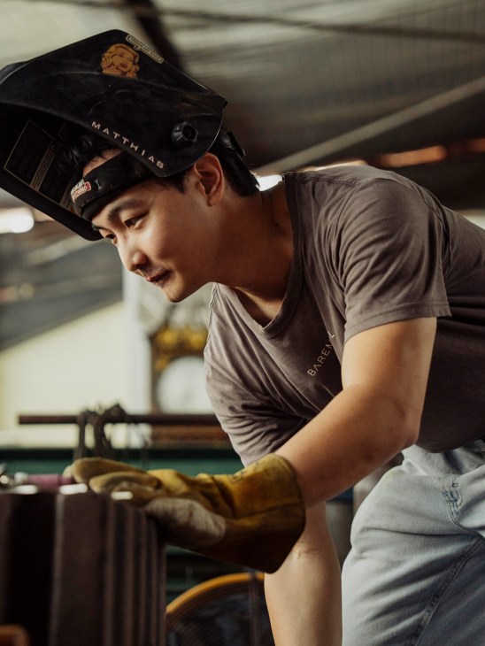 Metal artist Matthias Yong working in his workshop wearing protective gear and welding equipment.