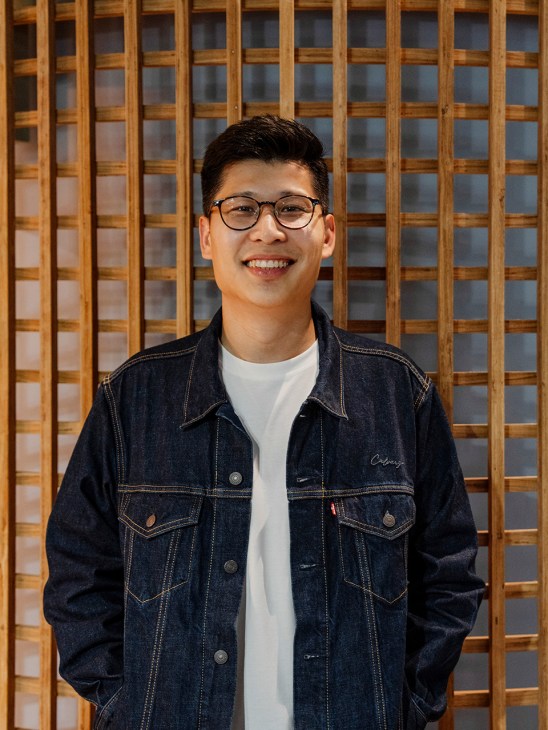 Hunn Wai, co-founder of Lanzavecchia + Wai, smiling in front of wooden lattice backdrop.