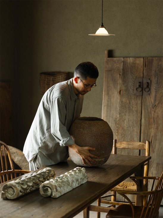 Gallerist Ryo Suzuki examines a large round Panari earthenware jar on a wooden table.