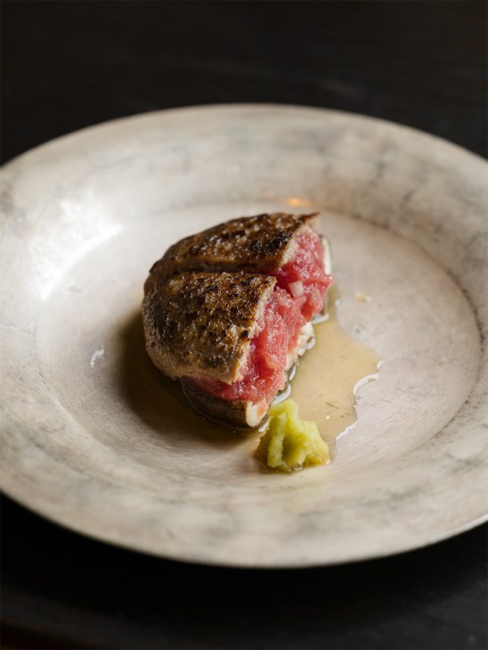 Seared tuna and shiitake mushroom dish plated on white marble plate with sauce and garnish