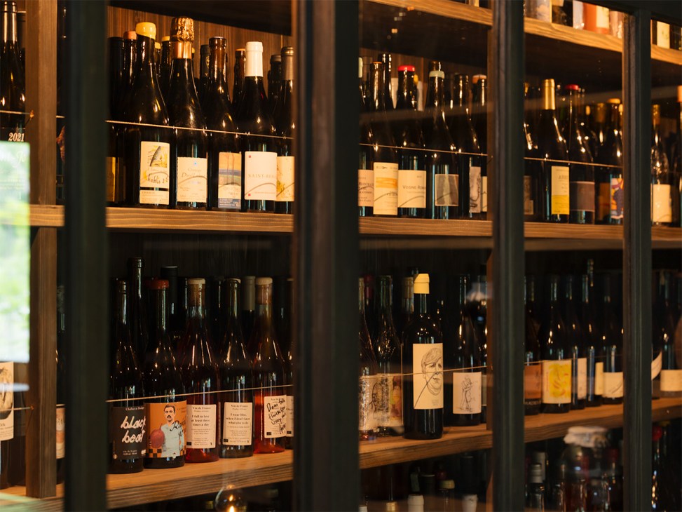 Wine bottles displayed on wooden shelves behind glass doors with warm lighting in Mube restaurant.
