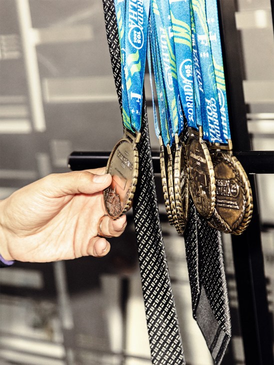 Hand holding multiple medals with blue ribbons from a 10k run organized by Folha de São Paulo.