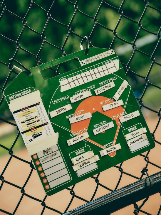Baseball lineup card and batting order sheet clipped to a chain-link fence at Heckscher Ballfields.