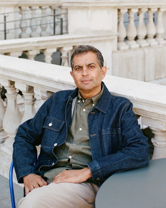 Man in denim jacket sitting against classical white stone balustrade backdrop