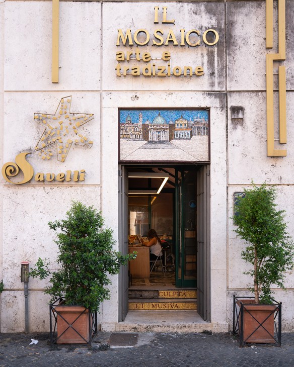 Savelli Religious storefront in Rome with golden signage, mosaic artwork above the entrance, and potted plants flanking the doorway.