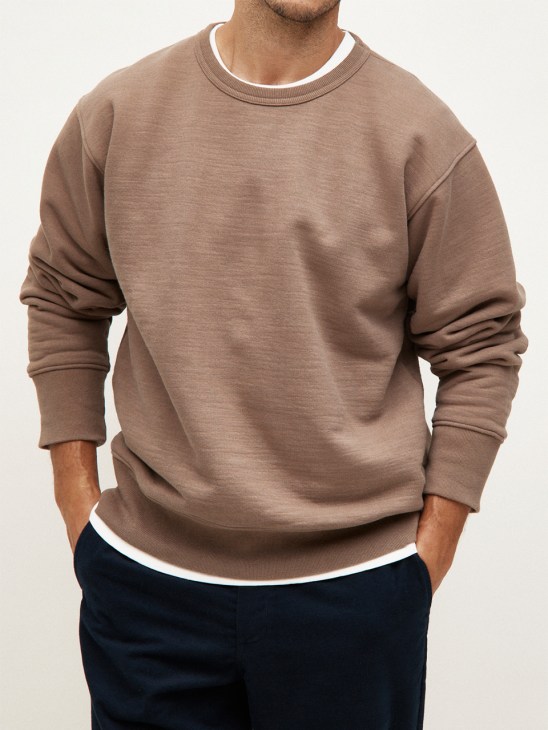 Man wearing taupe loopwheel crewneck sweatshirt with white trim and dark navy trousers.