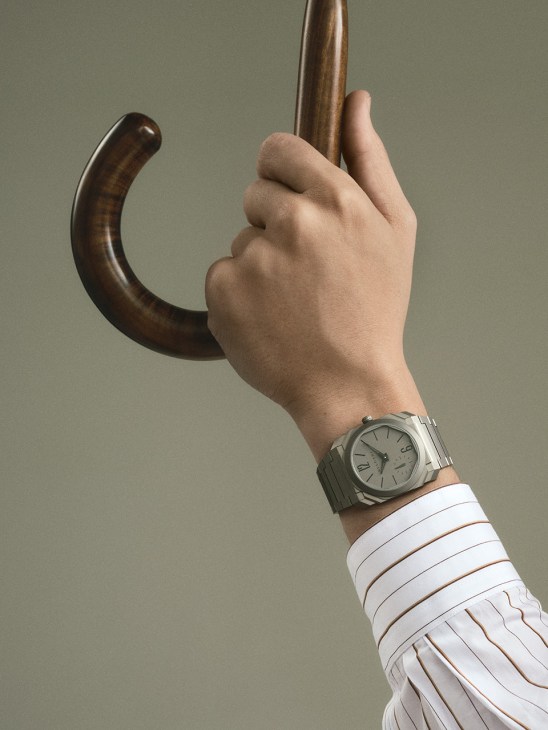 Hand holding a wooden umbrella handle wearing Octo Finissimo Automatic watch by Bulgari and white striped shirt by Graphpaper