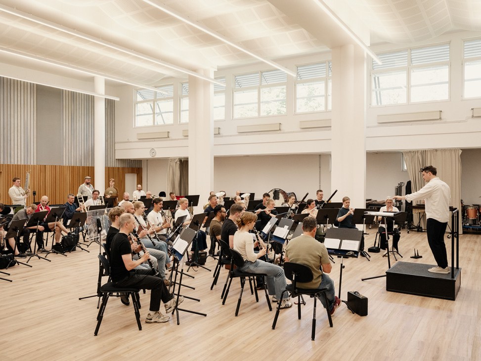 Major Eliasson conducts Swedish Army Band musicians during rehearsal in a bright, modern concert hall.