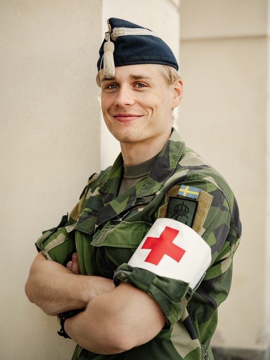 Swedish Army medic in camouflage uniform with red cross armband smiling at camera.