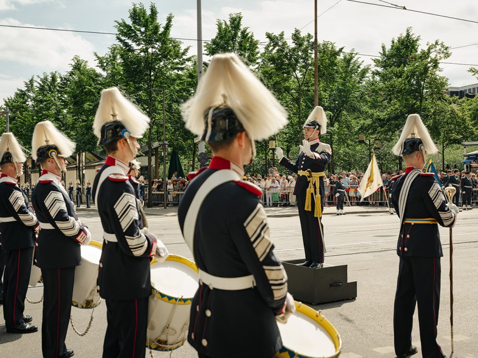 Swedish Army Band members in gunmetal-grey dress uniforms with tall white bearskin hats perform at a public ceremony.
