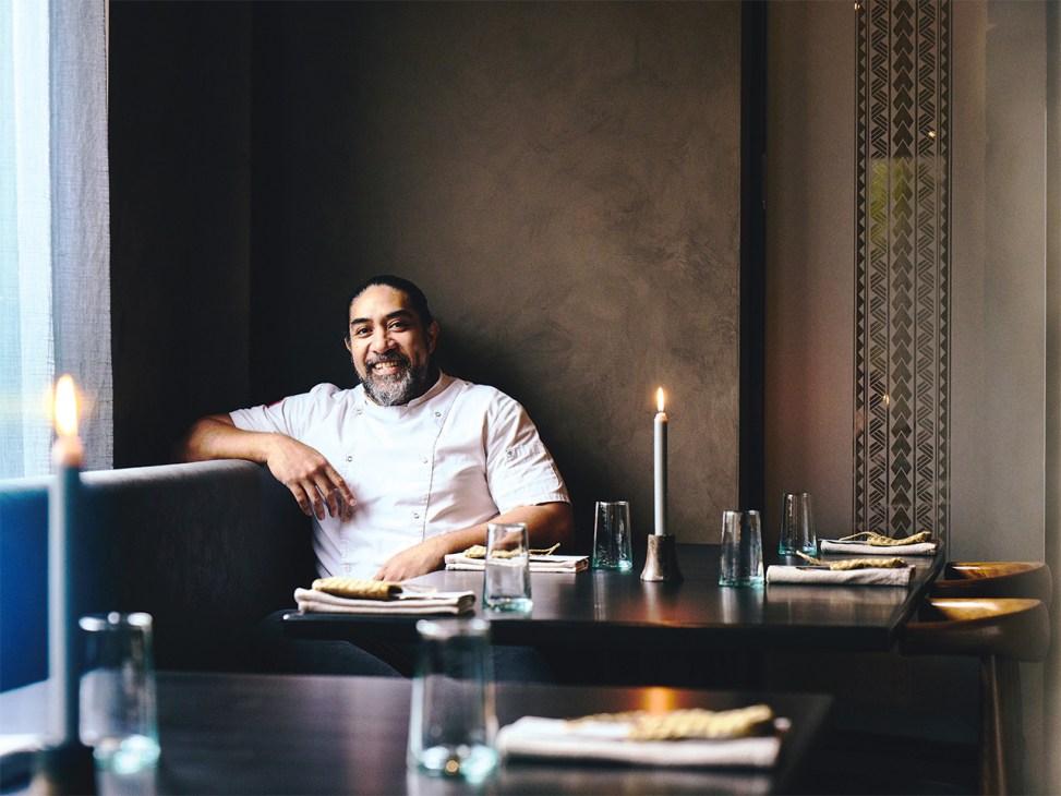 Chef Henry Onesemo smiling at a dining table set with candles and place settings at Tala restaurant