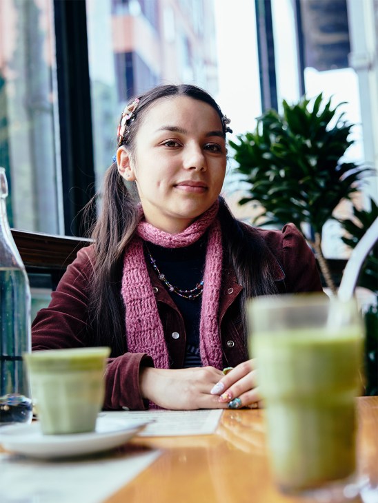 Fine art student Ngaio Dawson sitting at a café table with a matcha latte and green drinks.