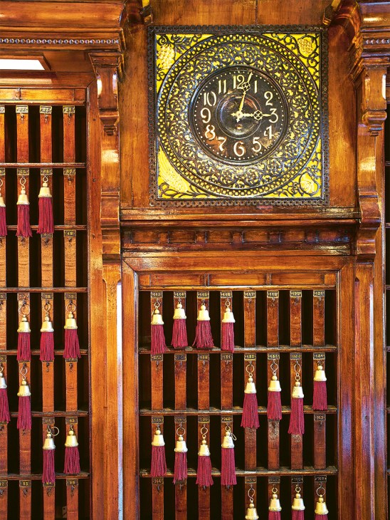 Ornate wooden cabinetry with brass keys and an antique clock with yellow face at the Danieli hotel concierge desk.