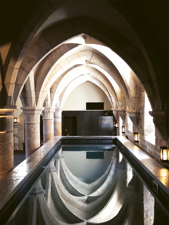 Underground vaulted stone archway with a rectangular pool reflecting the architecture at Les Sources de Vougeot hotel.