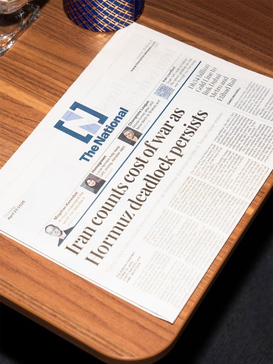A copy of The National newspaper lies on a wooden desk next to a blue patterned object.