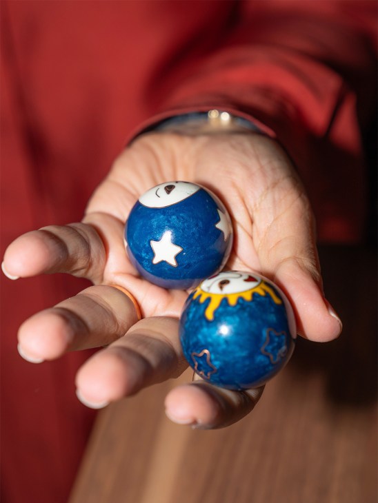 Hand holding three blue decorative stress balls with white star and eye designs and white ceramic tops.
