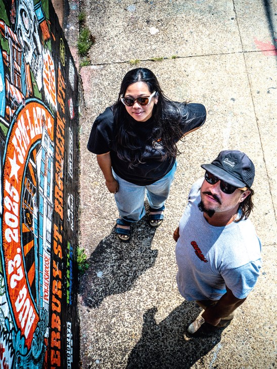 Two people standing on concrete ground next to colorful graffiti wall art, looking upward.