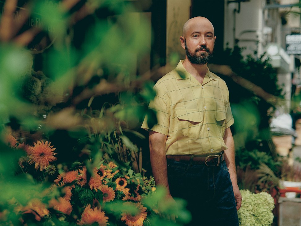 Man in yellow shirt standing among flowering plants in a garden setting.