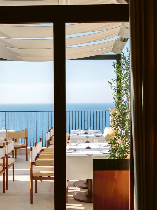 Gran Hotel Margalida's dining terrace overlooking the Mediterranean Sea with cream parasols and wooden chairs.
