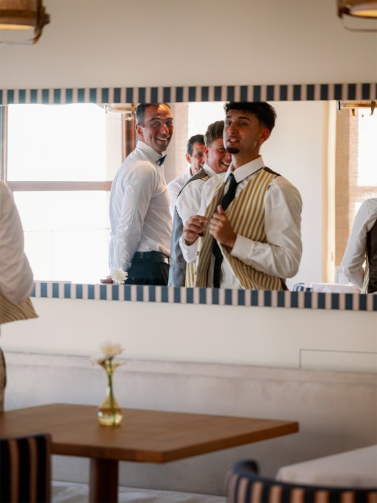Hotel staff in formal attire preparing for service, viewed through a mirror with blue striped frame.