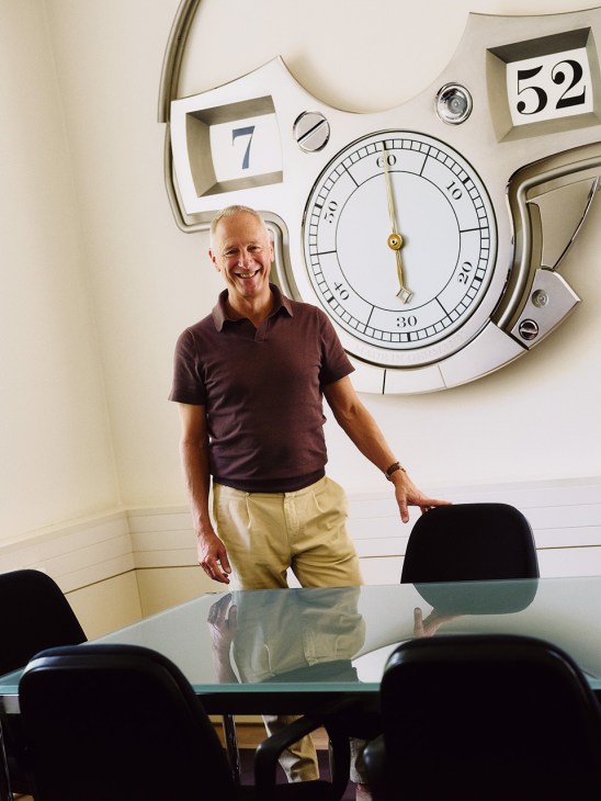 Wilhelm Schmid, CEO of A Lange & Söhne, smiling in an office with large vintage clocks and numbered panels on the wall.