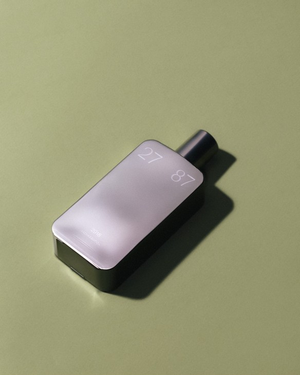 27 87 perfume bottle with purple-tinted glass and black spray top on pale green background.