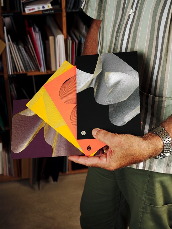 Person holding layered cardstock samples with colorful hot-foil stamping designs in yellow, orange, and metallic silver.