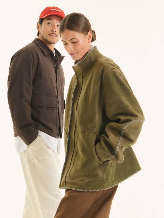 Man wearing brown Uniqlo blouson with red Monocle cap and woman wearing olive green Graphpaper jacket standing against white background