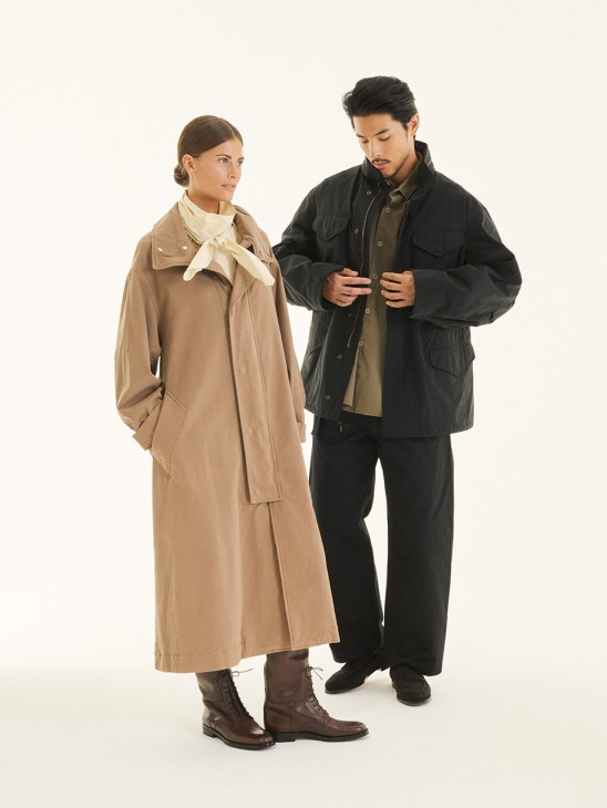 Woman in beige coat with cream scarf and man in black jacket over olive shirt standing together against white background.