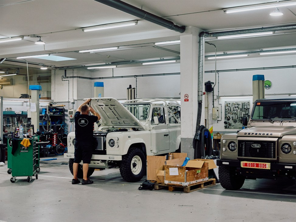 Mechanic working on a white Land Rover Defender in Costa Motor's workshop with additional vehicles visible