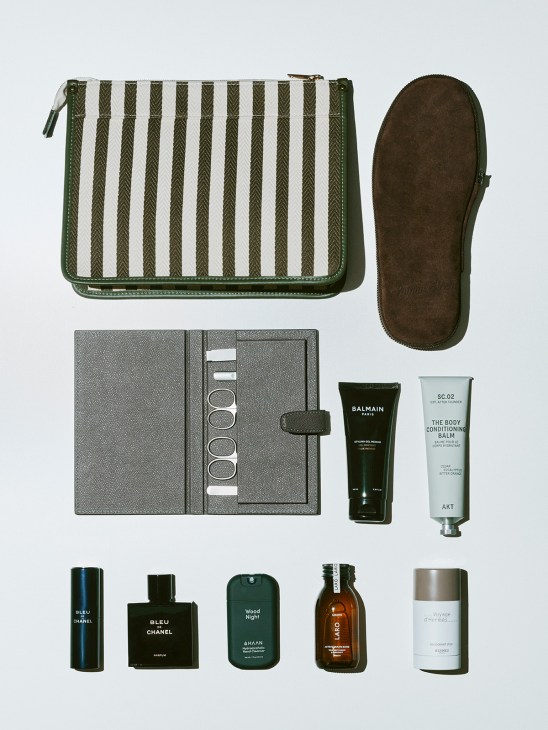 Travel accessories including striped pouch, slippers, manicure set, and beauty products by Balmain, AKT, Chanel, Haan, Laro and Hermès.
