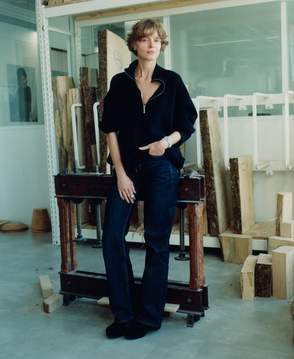 Priscilla Royer, creative director of Maison Michel, stands in a workshop surrounded by wooden hat molds and materials.
