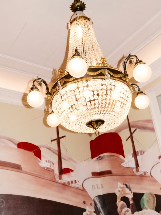 Ornate crystal chandelier with brass arms and globe lights hanging from white ceiling.