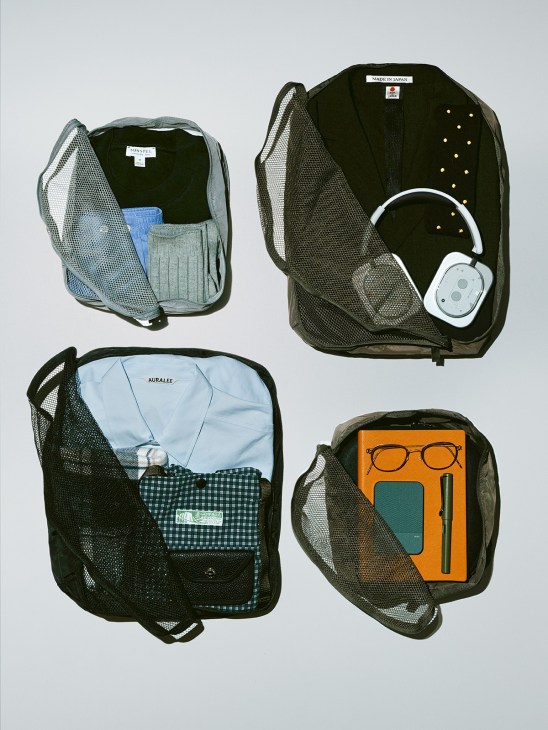 Four open packing cubes displaying folded clothing, accessories, and electronics including headphones and glasses.