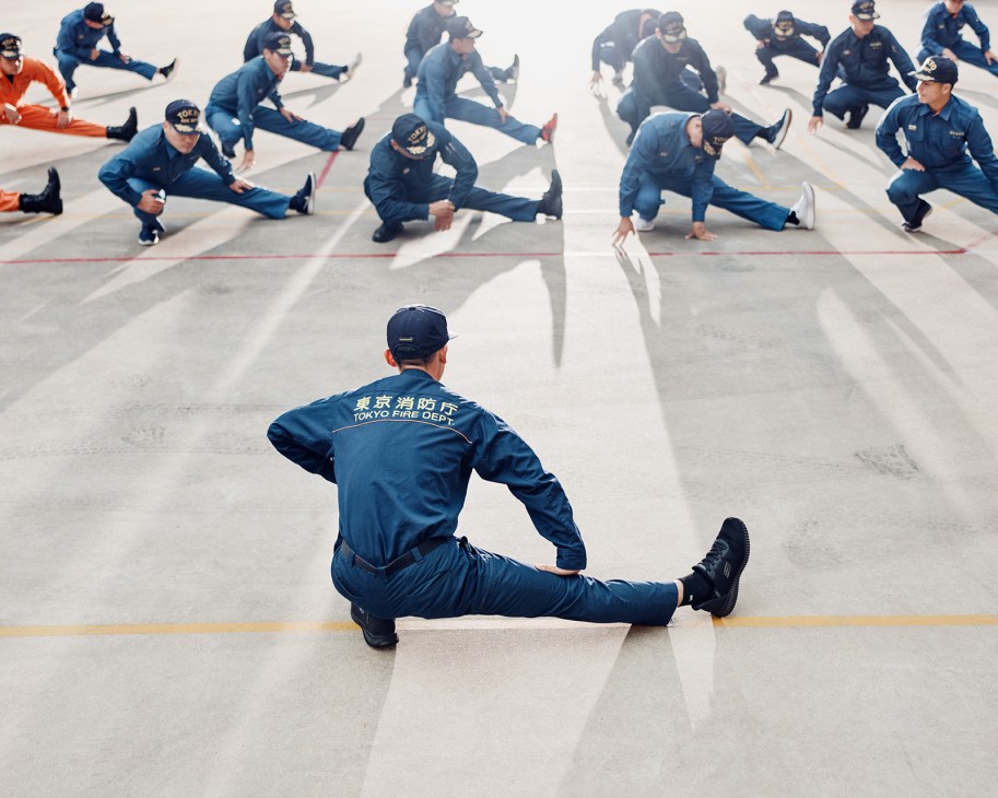 Tokyo Fire Department firefighters performing stretching exercises on the ground during a calisthenics training session.