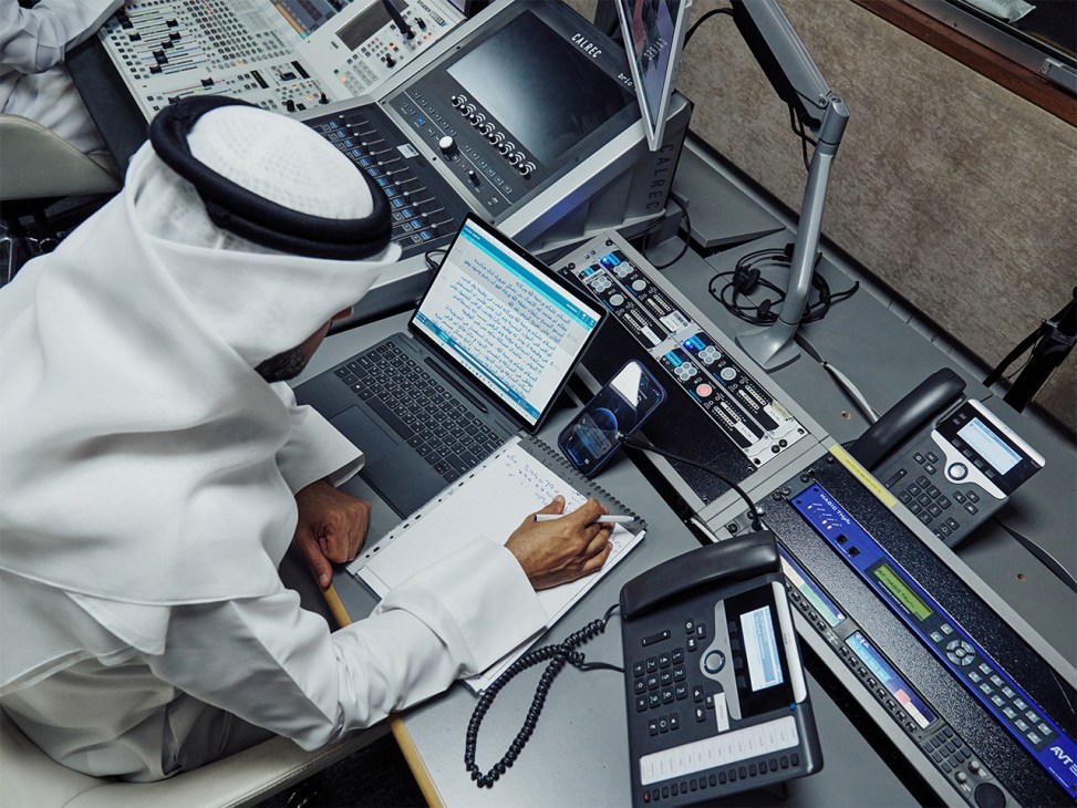 Radio producer in white kandura works at console during Al Khat Al Mubasher broadcast in Sharjah studio.