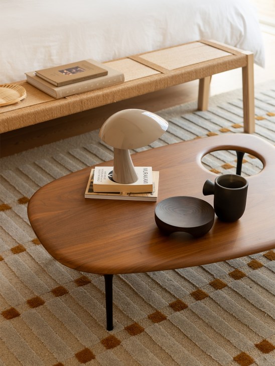 Wooden oval table with mushroom-shaped lamp, black ceramic bowl and pitcher, styled with magazines and books