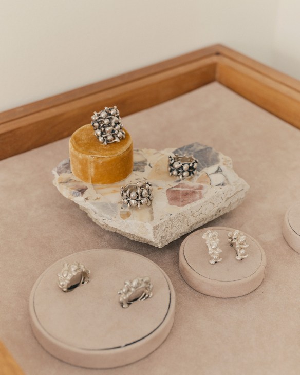 Handcrafted silver cluster rings displayed on cream-colored stands and a textured stone platform with wooden frame.