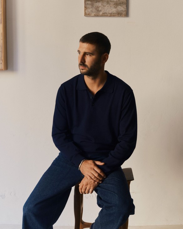 Man in navy shirt and jeans sitting on wooden chair in minimalist white gallery space
