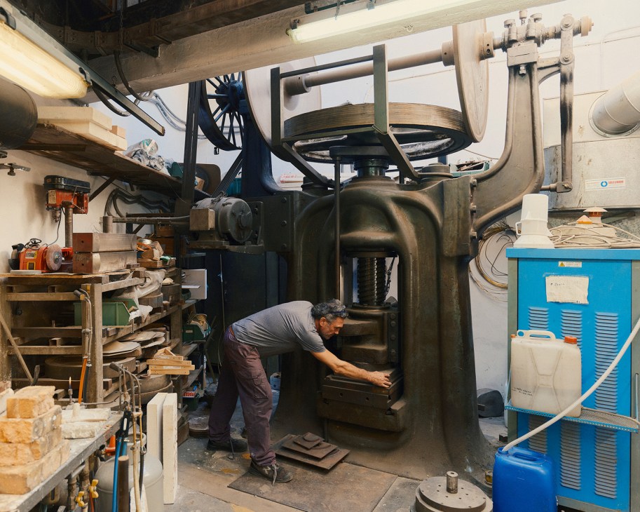 Craftsman operating large metal-shaping press equipment at Pampaloni workshop in Florence.