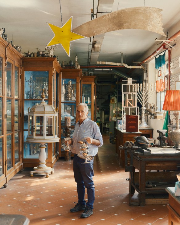 Gianfranco Pampaloni holds silver pieces in his family's Oltrarno workshop filled with wooden display cabinets and craft tools.