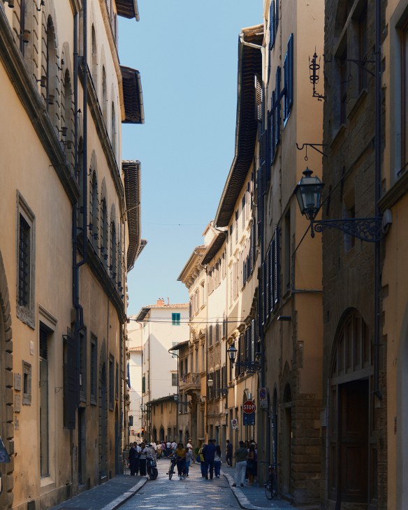 Narrow cobblestone street lined with historic ochre and beige buildings in Florence's Oltrarno district with pedestrians walking.