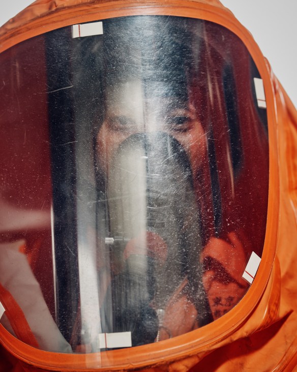 Firefighter wearing orange hazmat suit with large reflective visor covering face