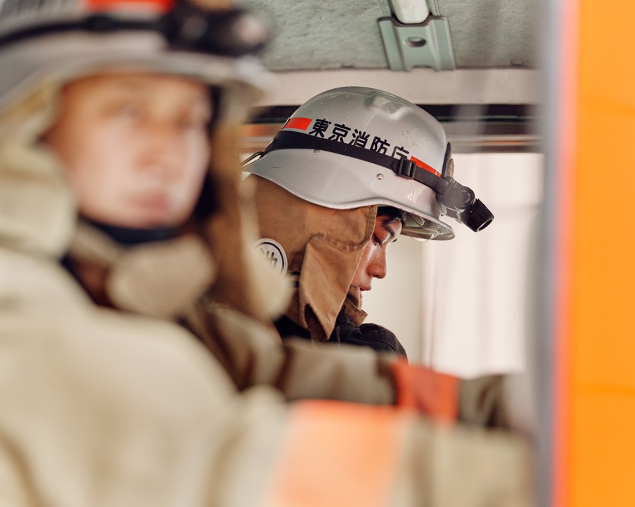 Tokyo Fire Department firefighters in training gear practicing quick entry into a fire truck during drills.